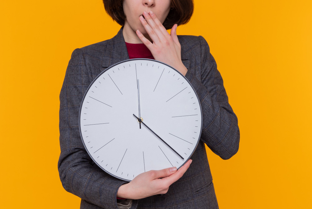 Žena s nástennými hodinami. Zdroj: magnific https://www.magnific.com/free-photo/young-woman-with-short-hair-wearing-grey-jacket-holding-wall-clock-looking-amazed-surprised-covering-mouth-with-hand-standing-orange-wall_13099224.htm#fromView=search&page=5&position=0&uuid=733c3973-4237-4c98-b9c3-d81a7ffb6860&query=time+running+out